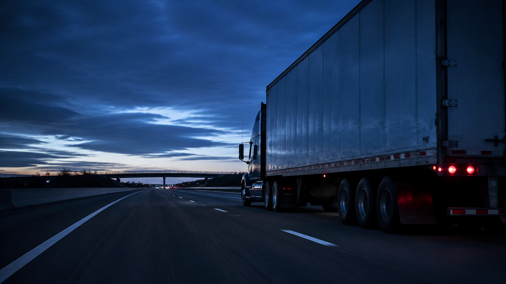 Camión con tráiler circulando por una autopista interestatal al anochecer.